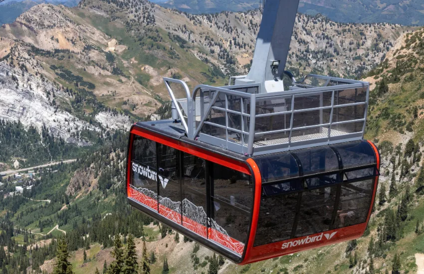 Red aerial tram cabin climbing above peaks